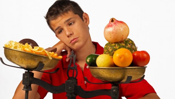 Парень и весы с фастфудом и фруктами/овощами