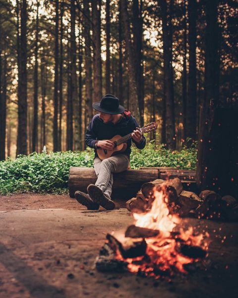 Парень в лесу играет на укулеле у костра