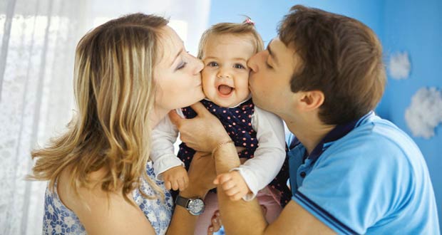 Молодые родители целуют свою дочку