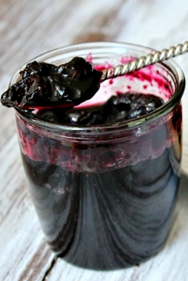 jar of blueberry jam open with a spoon inside and jam on the spoon sitting on the top