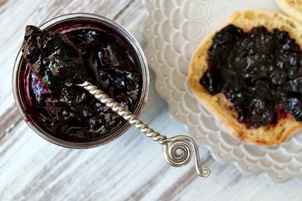overhead shot of Homemade Blueberry Refrigerator Jam in a jar with a spoonful of jam sitting on top. english muffin with jam on a plate alongside